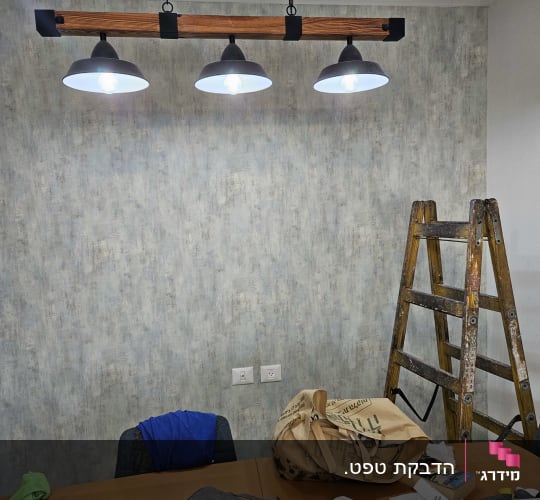 קיר עם טפט אפור, סולם ועבודות נייר על שולחן